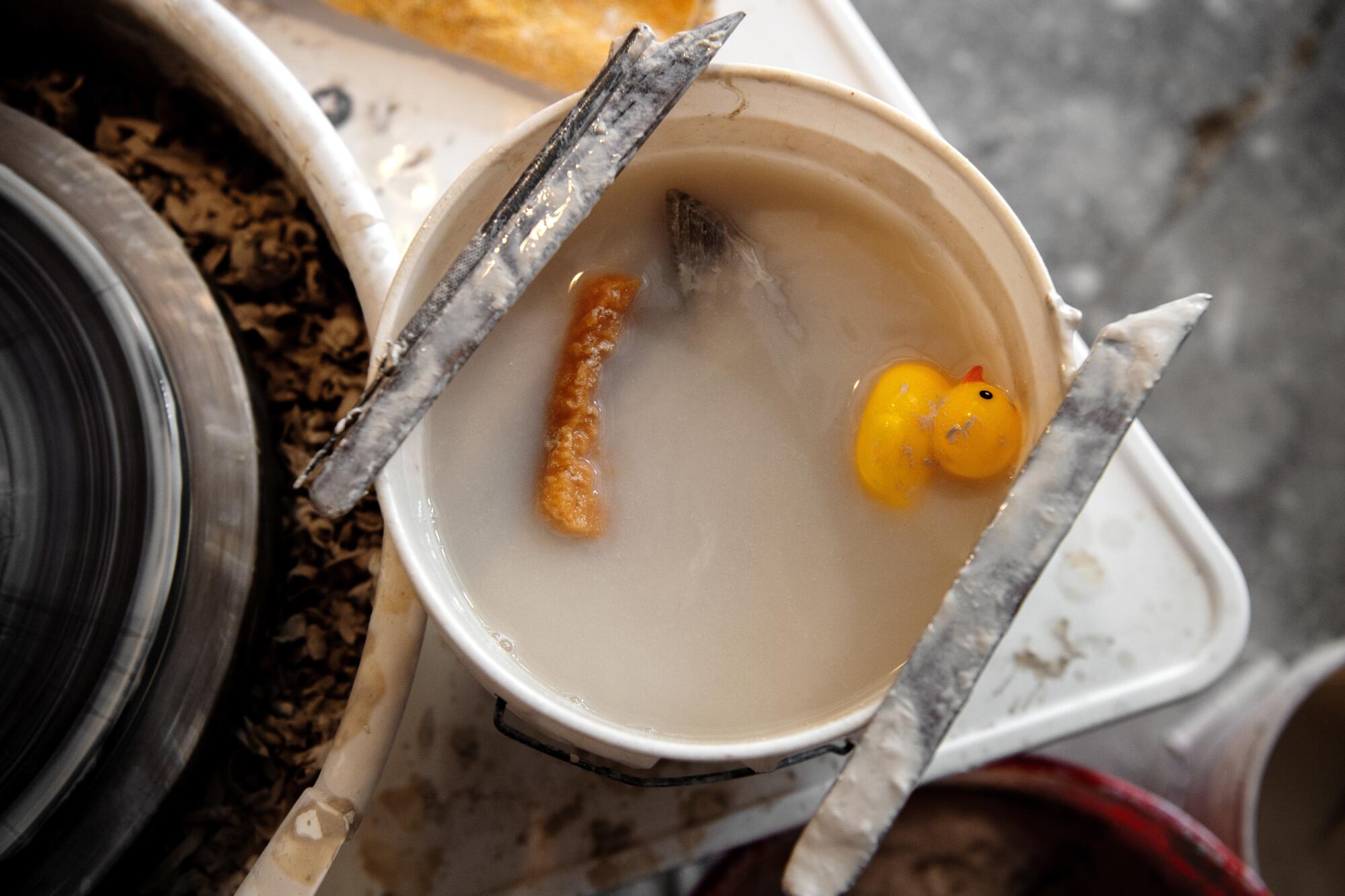 A rubber duck floating in clay-clouded water next to a pottery wheel.