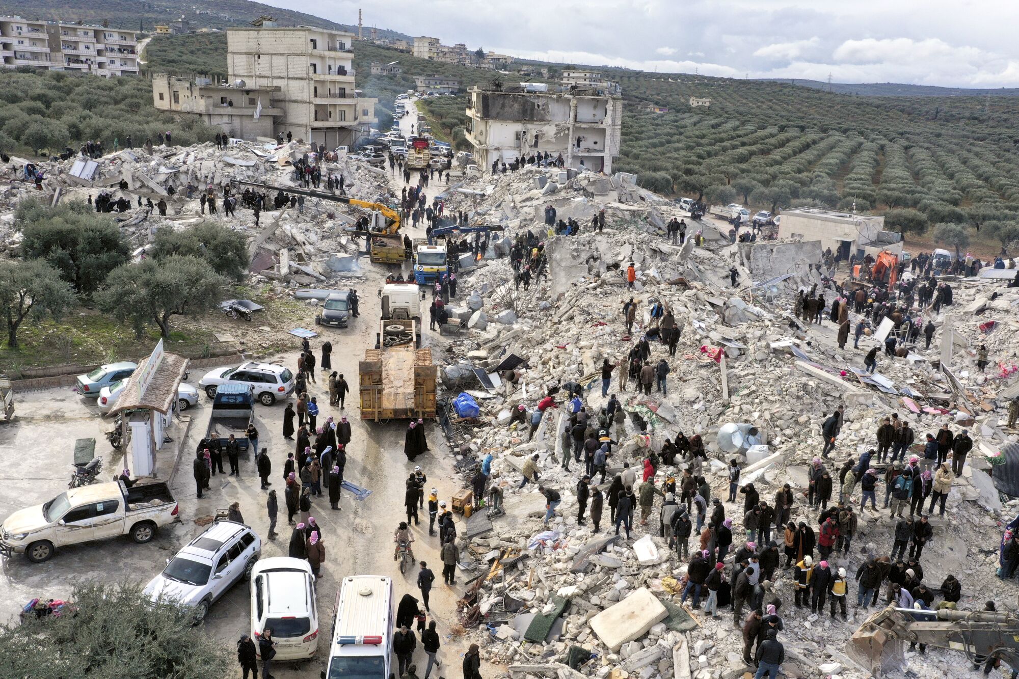People stand atop a pile of collapsed buildings as they search through the rubble.