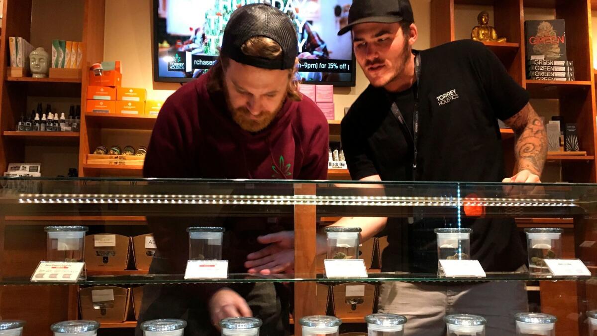 Torrey Holistics employees Matt Sullivan, left, and Taron McElroy arrange jars of cannabis in San Diego earlier this month. The first license for recreational retail sales went to Torrey Holistics.