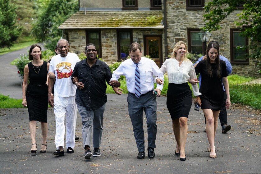 Bill Cosby and others, with arms linked, approach members of the media gathered outside Cosby's home. 