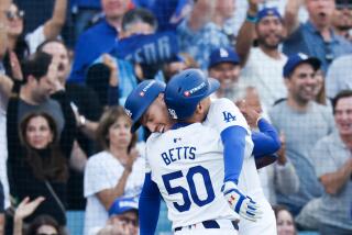 Dodger Mookie Betts hugs teammate Freddie Freeman, helping injured Freeman come to a stop after crossing home plate.