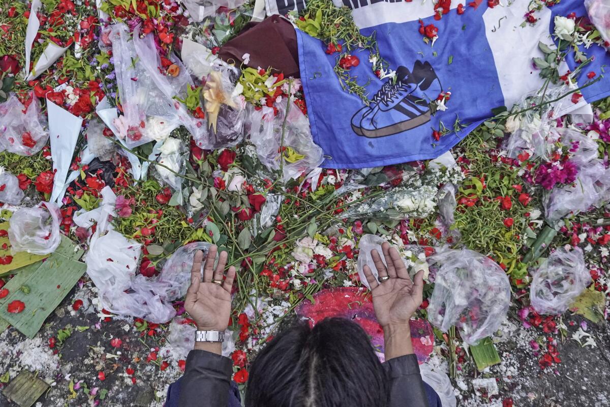 A man prays near flowers laid at the Kanjuruhan Stadium where a soccer stampede killed more than 100 people on Oct. 1, in Malang, East Java, Indonesia, Saturday, Oct. 8, 2022. Indonesia's president said the country will not face sanctions from soccer's world governing body and will remain the host of next year's U-20 World Cup after the firing of tear gas after a match inside the half-locked stadium caused the deadly crush at the exits. (AP Photo/Dicky Bisinglasi)