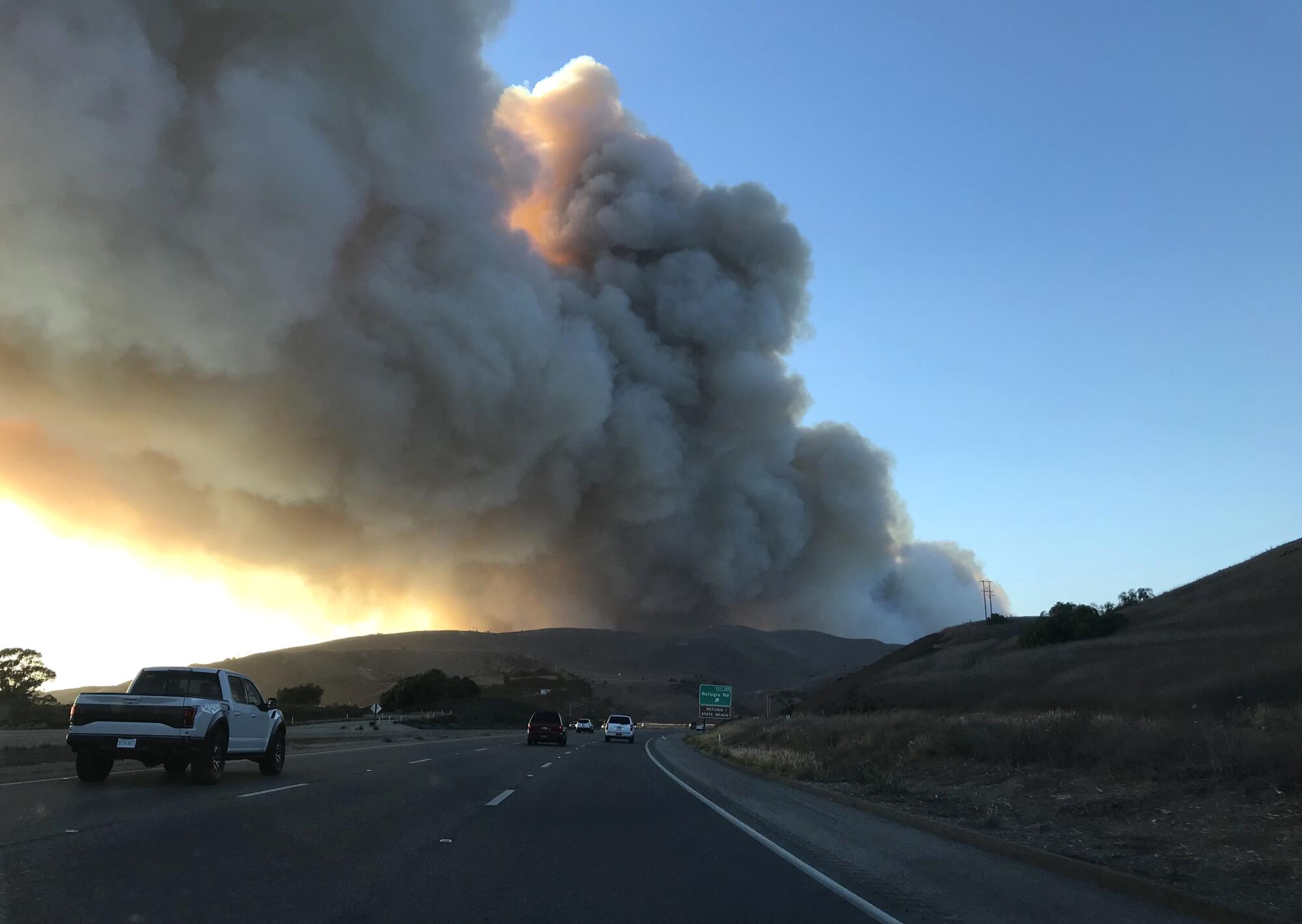 Cars on a highway, with smoke in the distance.