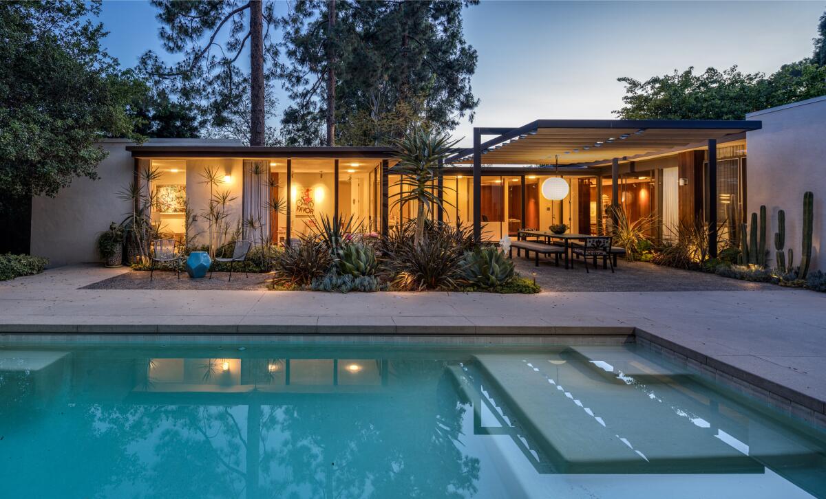 Across a swimming pool is a home with a wall of glass windows and covered patio area.