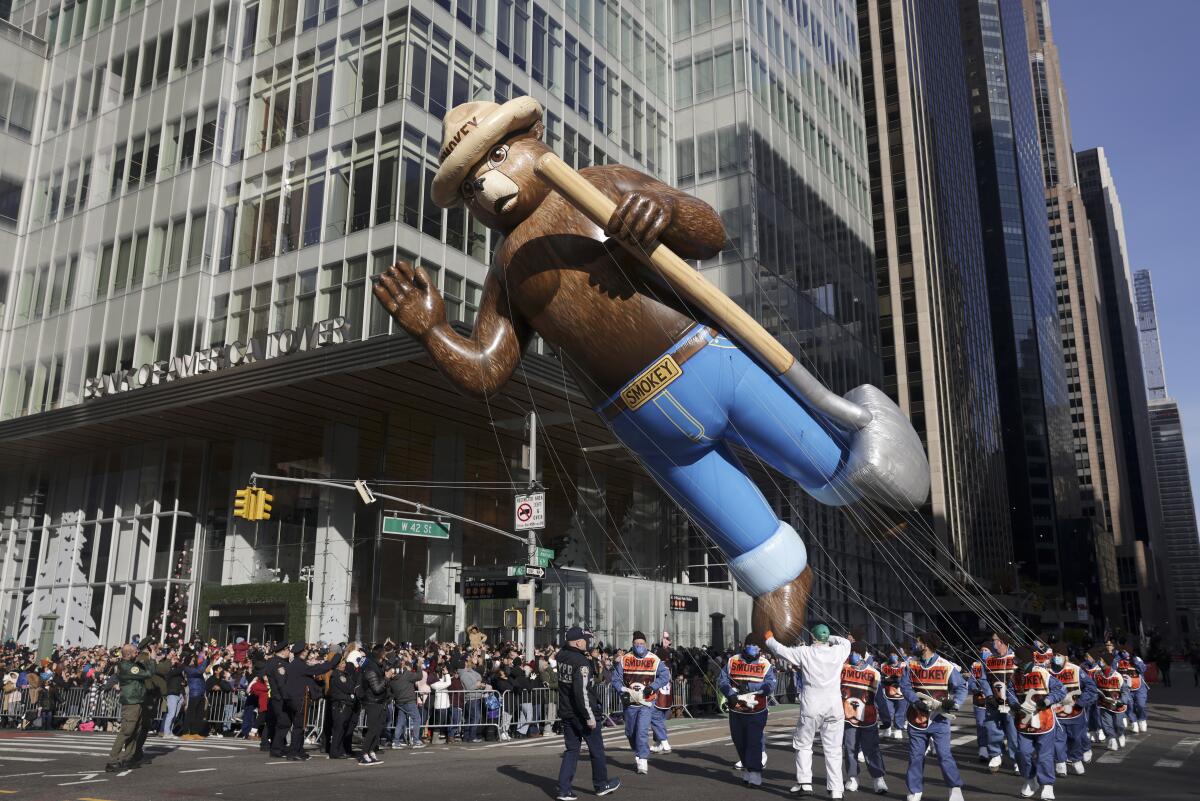 A giant floating bear balloon is handled by people during a parade.