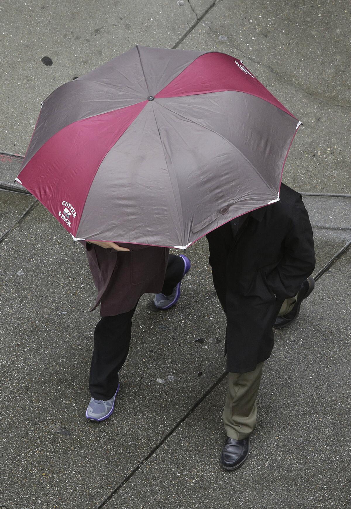 A woman and man walk under an umbrella as they cross a street in San Francisco on Thursday.