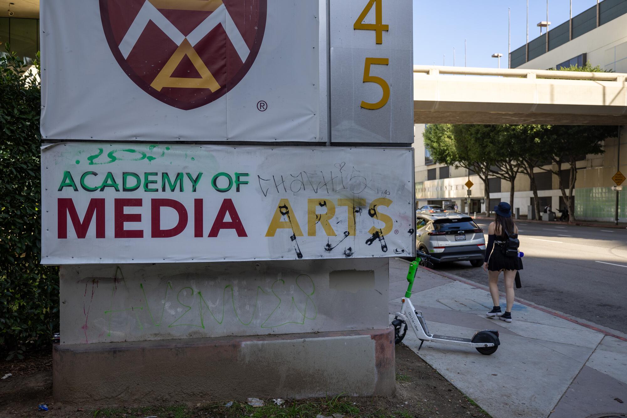   Graffiti sur une pancarte scolaire, détritus et scooter abandonné devant l’école Académie des arts médiatiques.