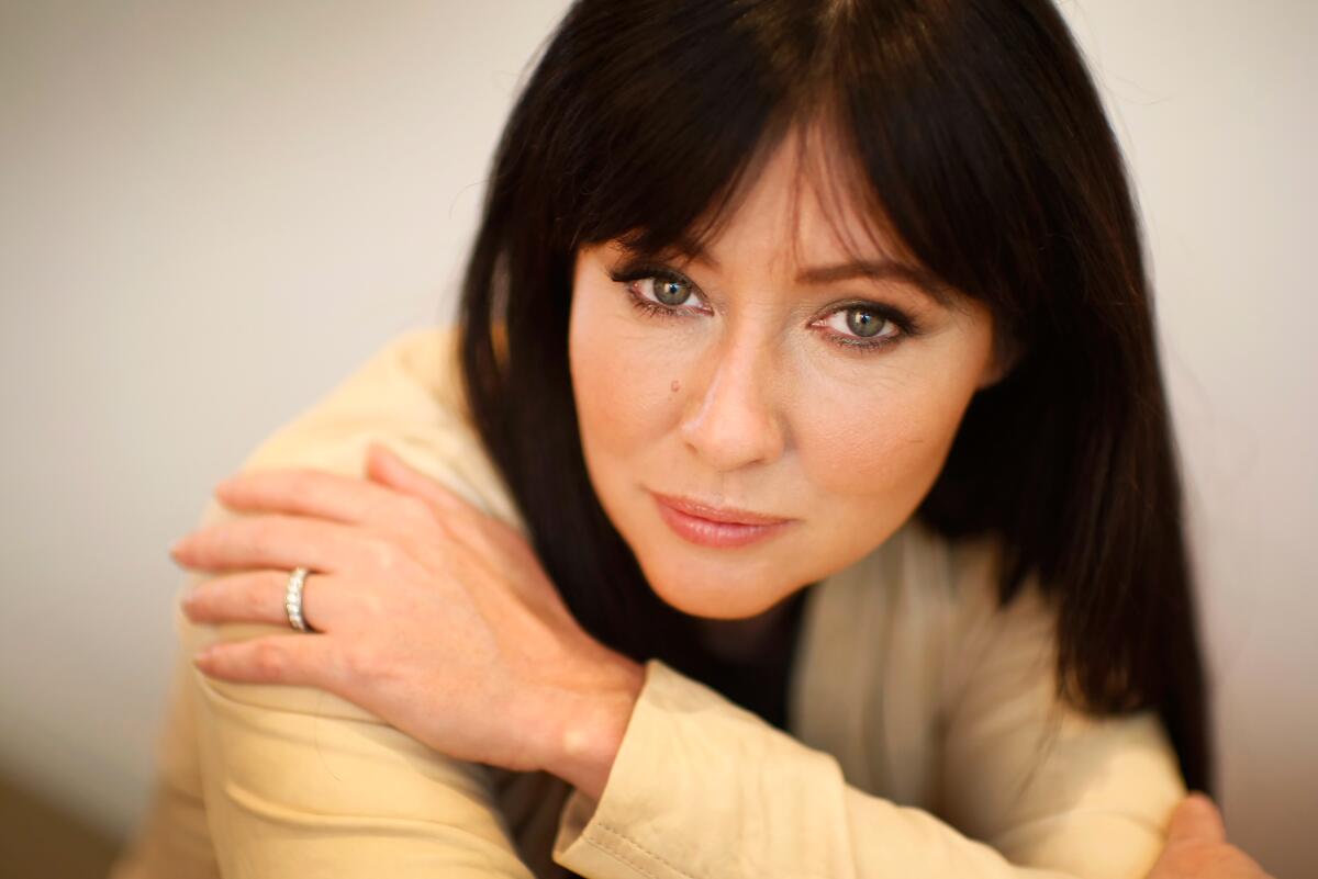 Shannen Doherty leans forward on folded arms.