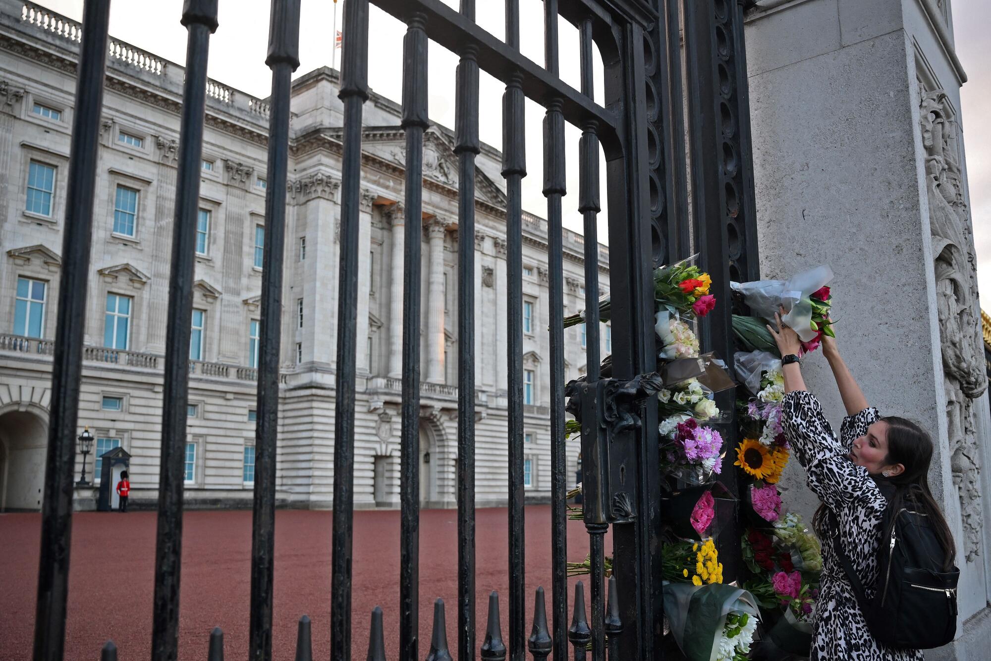 A woman tucks flowers into the gate outside Buckingham Palace in central London.