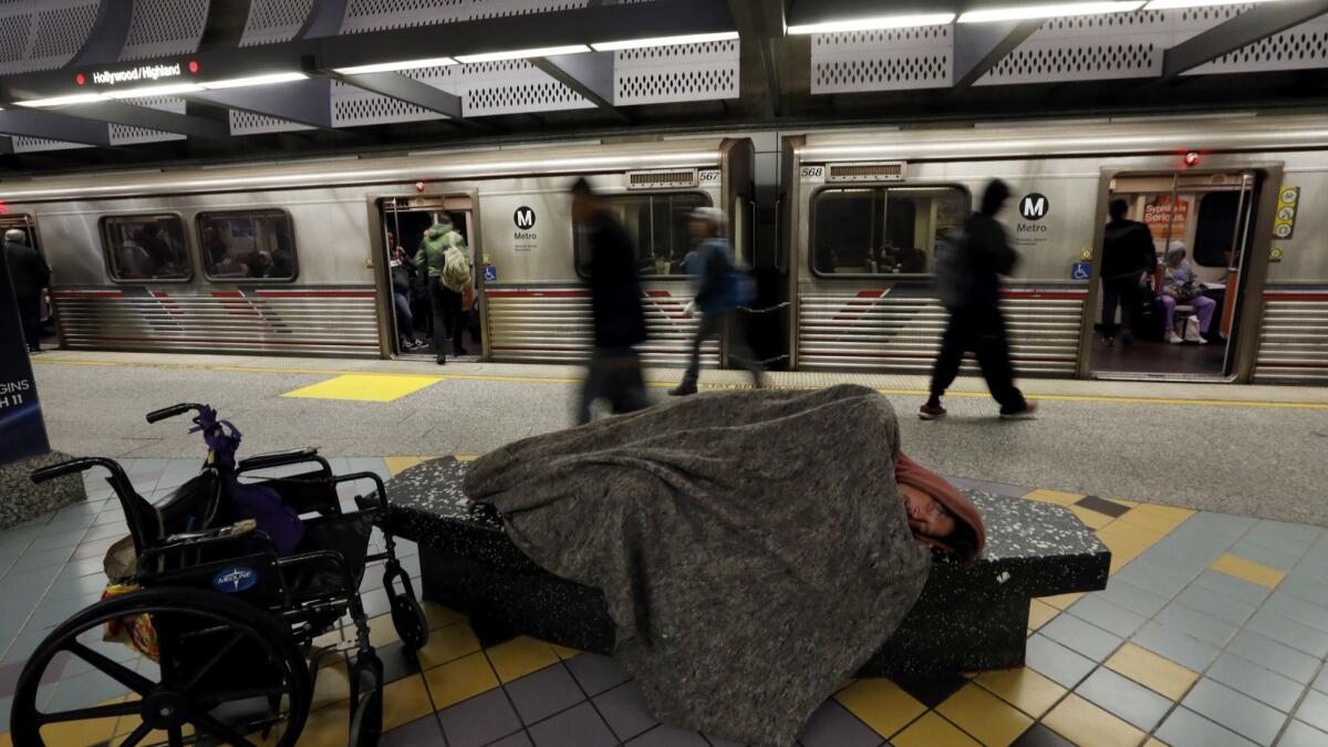 A man sleeps next to a wheelchair as morning commuters exit the Red Line at the Hollywood/Highland station. (Francine Orr / Los Angeles Times)