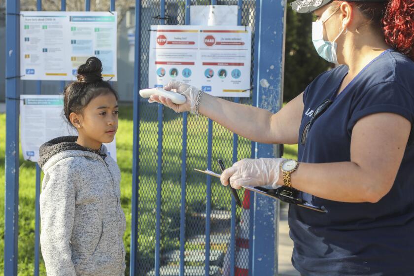 Natalie Perez (right) takes the temperature of Emily Lucatero (left), 9, before entering Chase Avenue Elementary School during the Cajon Valley Union School District's Emergency Child Care Program on May 5, 2020 in El Cajon, California. The district is offering free child care to essential workers.