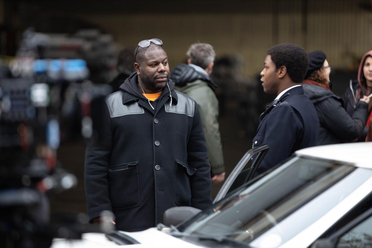 Director Steve McQueen talks to actor John Boyega standing next to a car.