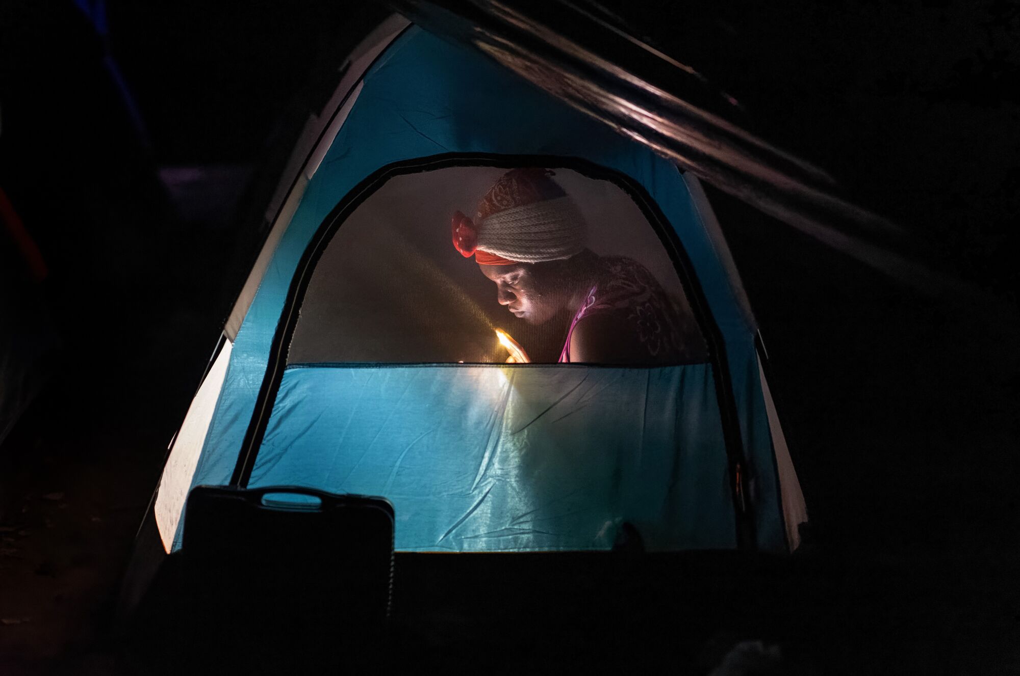 A Haitian immigrant is seen through the window of a tent at night.