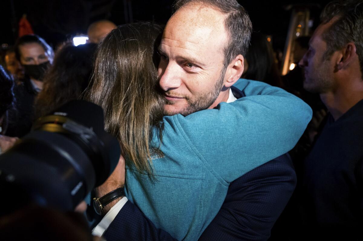 A man surrounded by a crowd and cameras is hugged by a woman.
