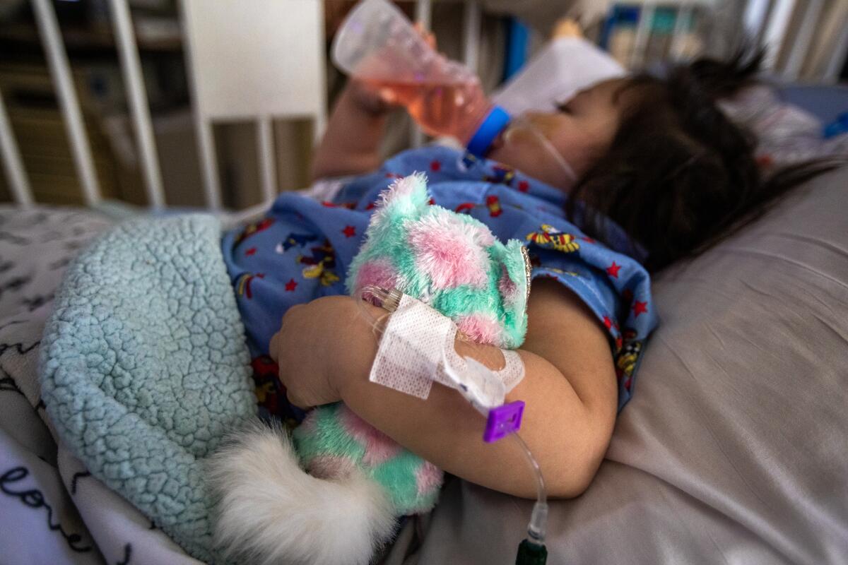 A toddler drinks juice in a hospital.
