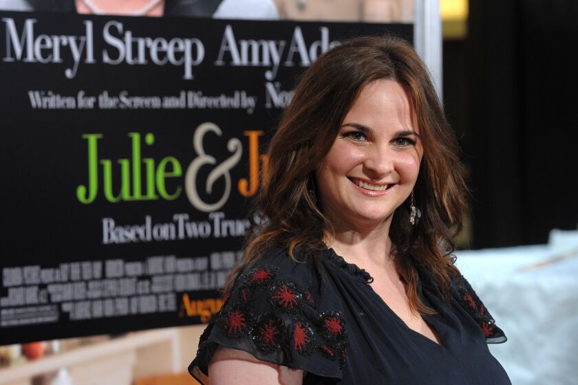 A woman with long brown hair wearing a black dress and smiling