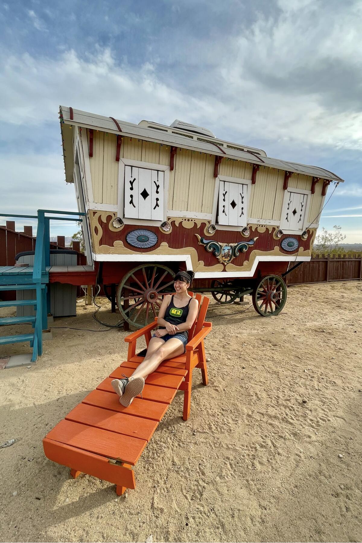 A woman relaxes on a lounge chair in front of a wagon.
