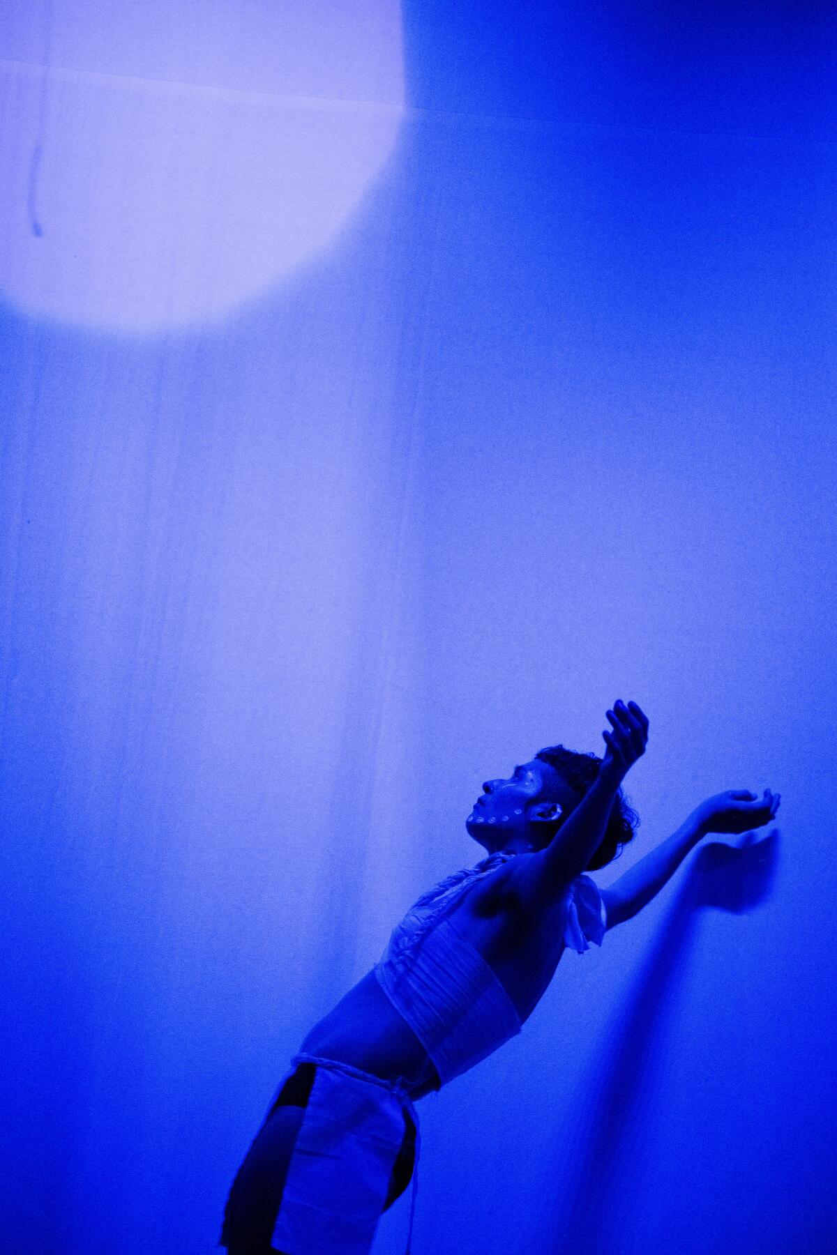 A blue-tinted image shows a dancer, with arms extended toward upward.