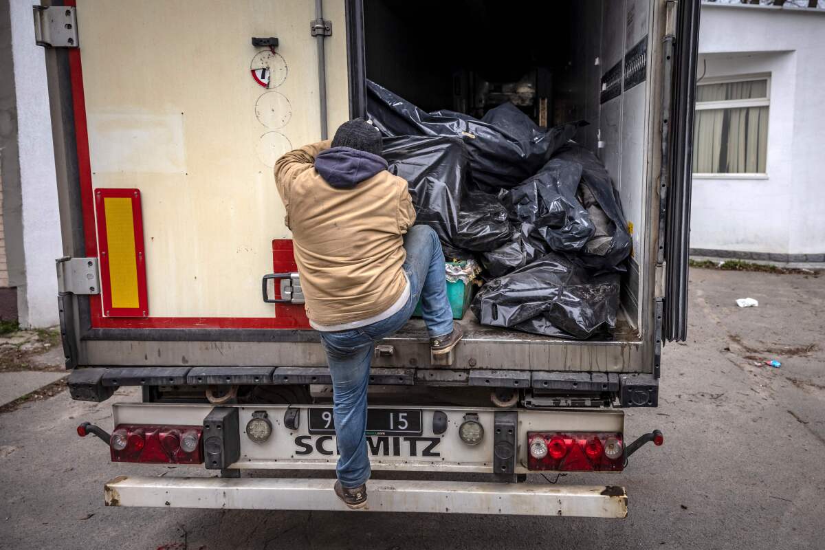 A man at the back of a truck filled with black bags.