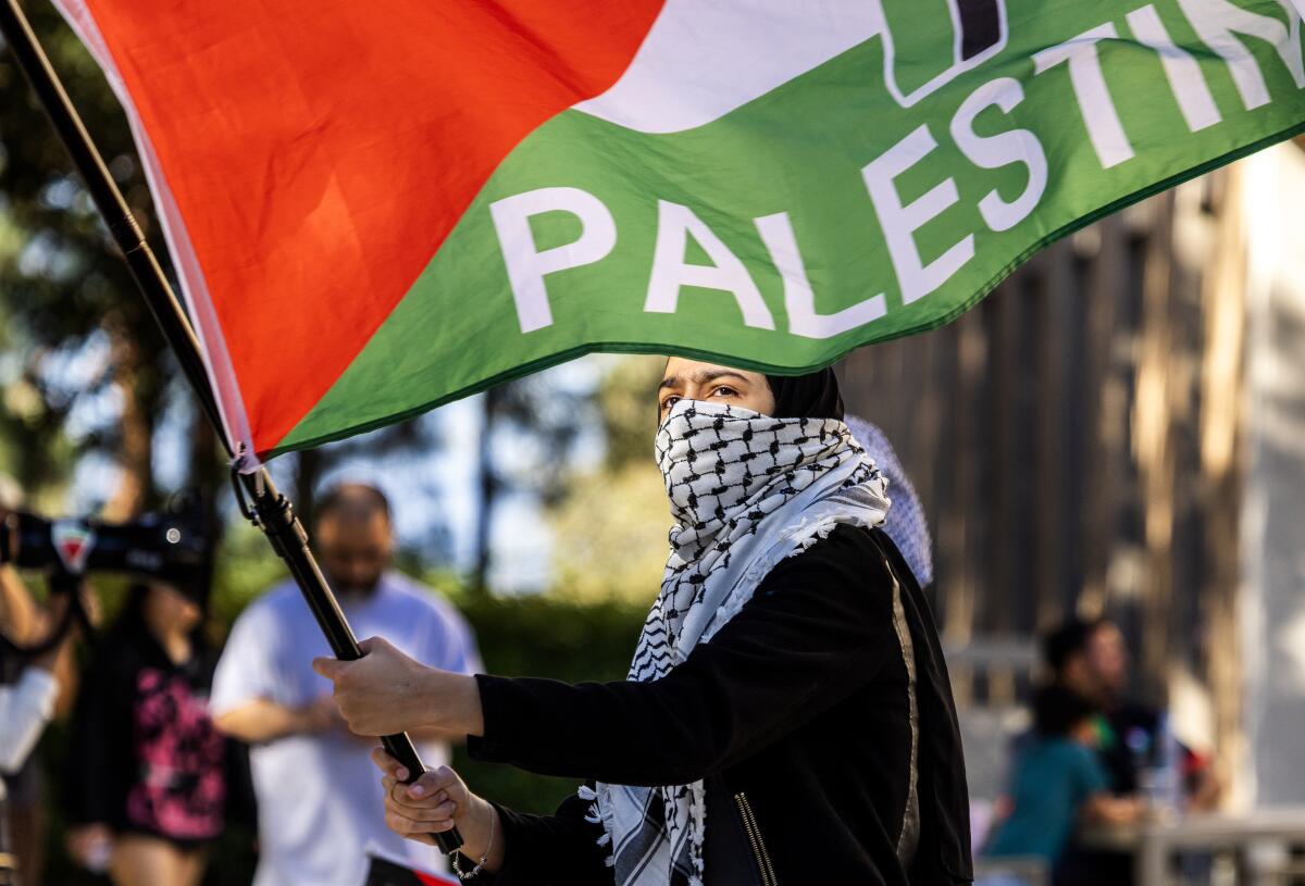 A protester carries a Palestinian flag in solidarity with a pro-palestinian encampment nearby on the UC Irvine campus