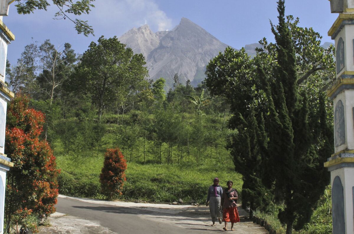 FILE - In this May 11, 2018, file photo, villagers walk along a road Mount Merapi is seen in the background in Pemalang, Central Java, Indonesia. Indonesian authorities are raising the danger level for the volatile Mount Merapi volcano on densely populated Java island and ordering a halt to tourism and mining activities. (AP Photo/Agung Nugroho, File)