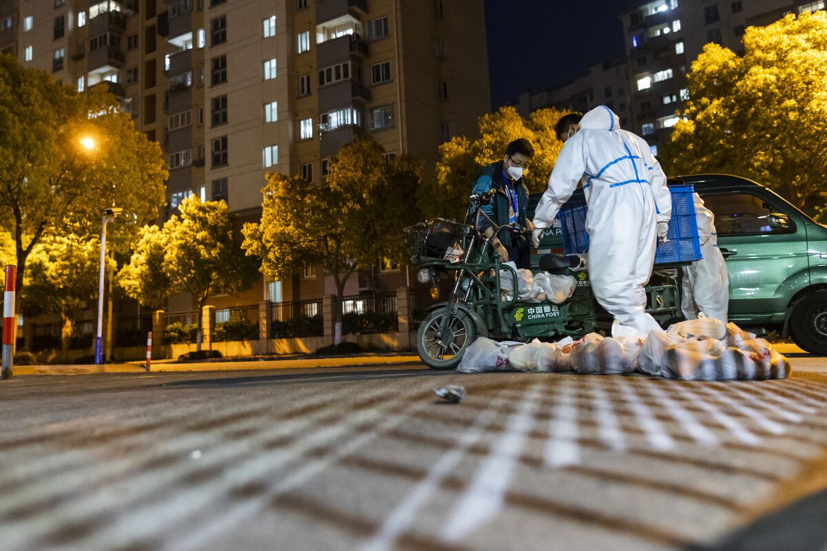 Deliverymen wearing protective suits carry bags of food at the gate of a residential community in Shanghai, China
