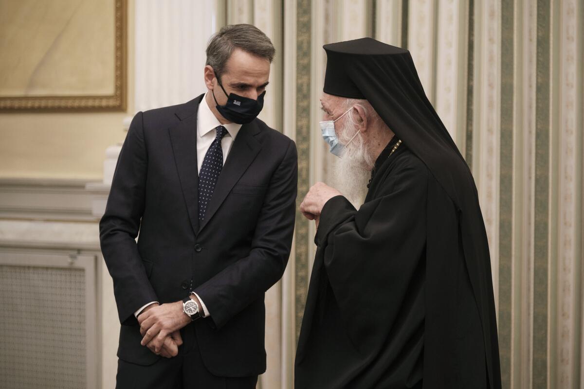 In this photo provided by the Greek Prime Minister's Office, Greece's Prime Minister Kyriakos Mitsotakis, left, talks with Archbishop of Athens and All Greece Ieronimos during a swearing-in ceremony of the new cabinet at the Presidential Palace in Athens, Tuesday, Jan. 5, 2021. Greece's powerful Orthodox Church is rebelling against a government order to briefly close places of worship under a weeklong drive to tighten virus restrictions before the planned reopening of schools. The conservative Church's ruling body issued a statement Monday directing priests to admit worshippers during indoor services for Wednesday's feast of the Epiphany. (Dimitris Papamitsos/Greek Prime Minister's Office via AP)