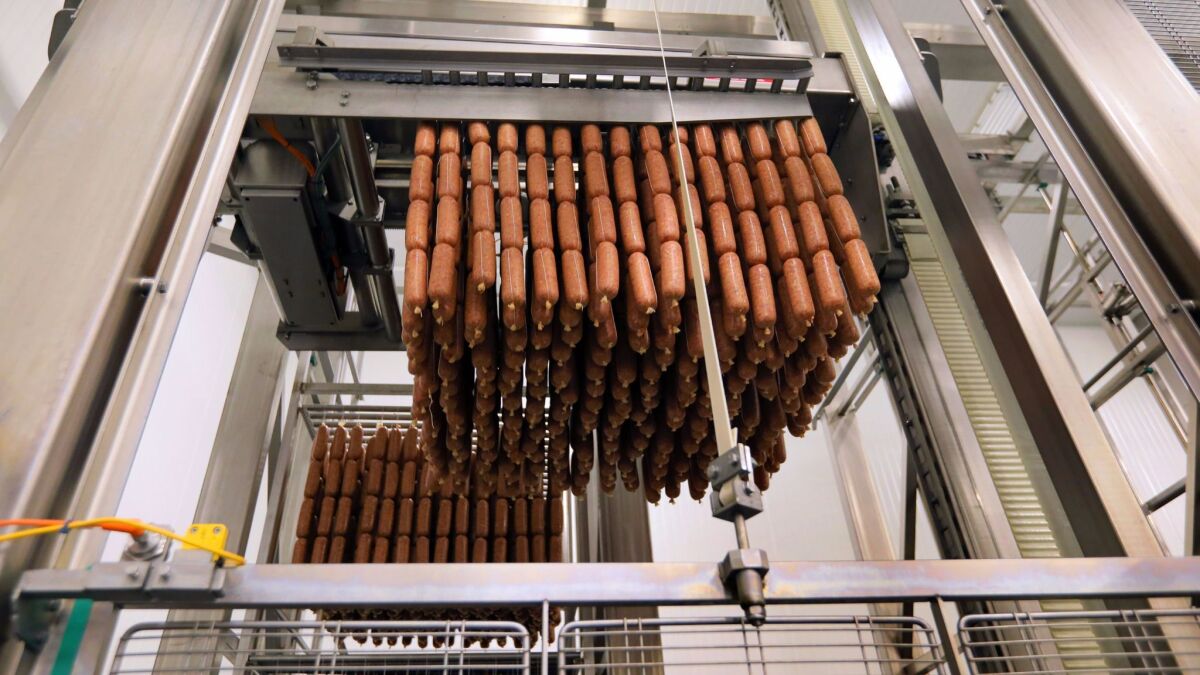 A machine lifts freshly-stuffed raw salami into racks that will be sprayed with a fermenting mold and chilled for a week before they move to curing rooms to dry at Olli Salumeria in Oceanside.