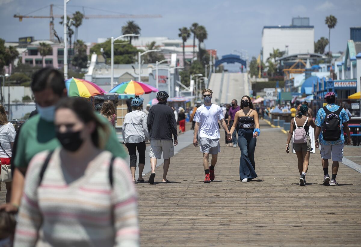 People wear protective face coverings during their strolls Monday on the Santa Monica Pier.