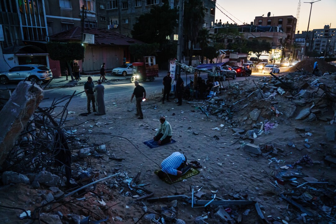Les hommes palestiniens entourés de décombres prient après le coucher du soleil.