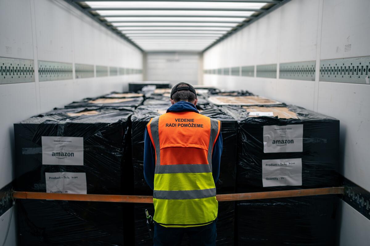 An Amazon worker readies humanitarian supplies for Ukraine. Large boxes wrapped in black are piled up and tied down.