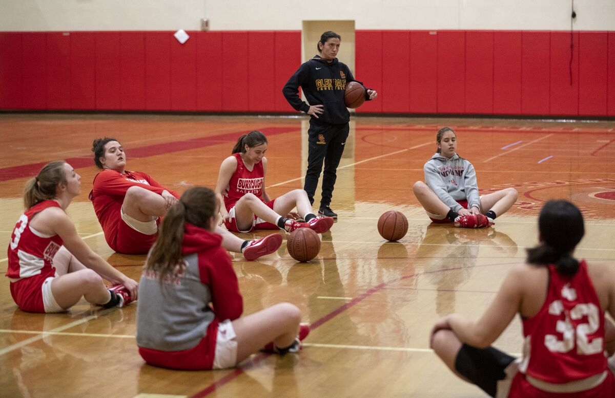 Burroughs girls basketball coach Vicky Oganyan stands while her team stretches for a late evening practice in the school gym on Feb. 12.