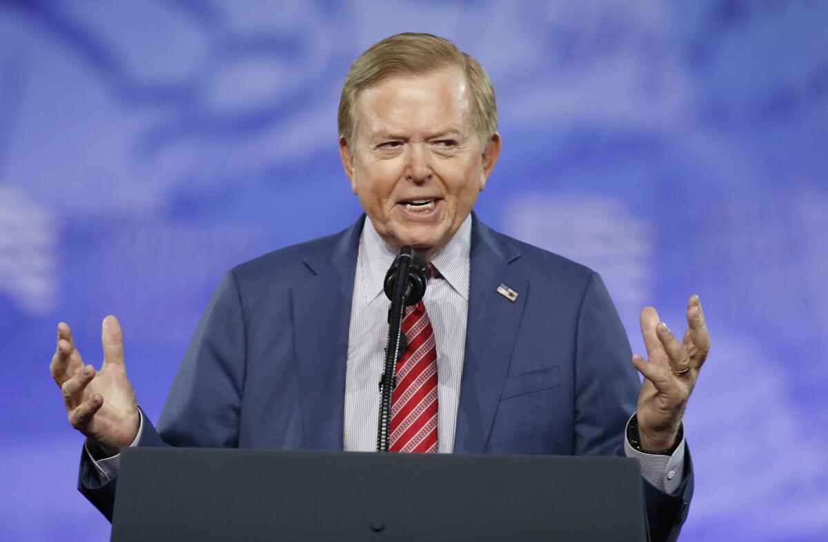 Lou Dobbs speaks into a microphone while gesturing with his hands