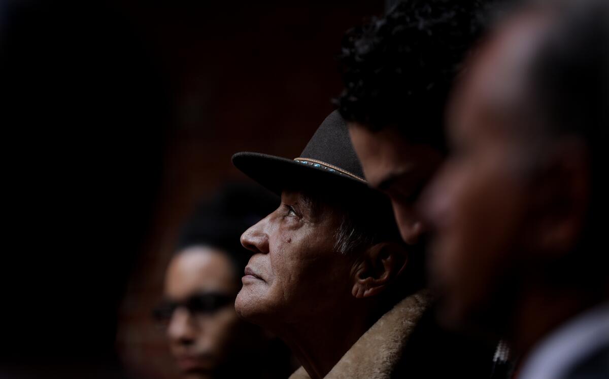 Against a dark background, a man in a hat looks up.