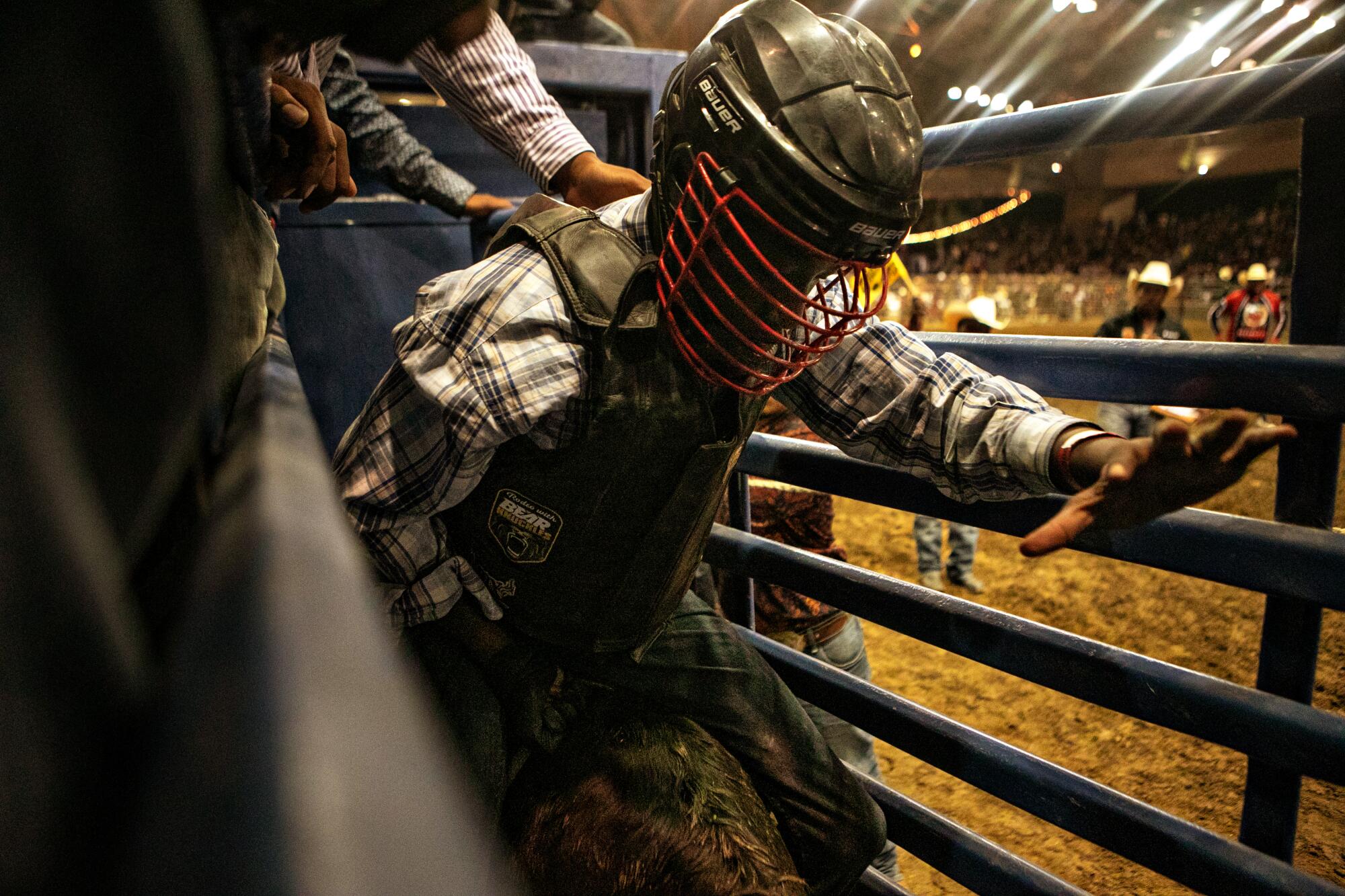 Hands reaching down to help boy in a helmet settle on to a bull in a chute