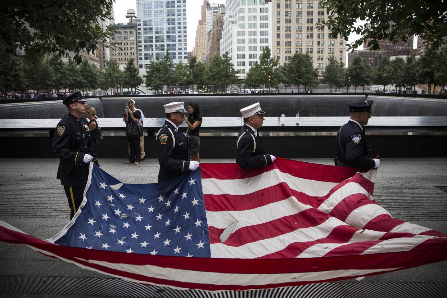 Members of the New York Police Department, Fire Department of New York and Port Authority Police Department carry an American flag damaged in the 9/11 attack at the beginning of commemoration ceremonies at the site of the World Trade Center.