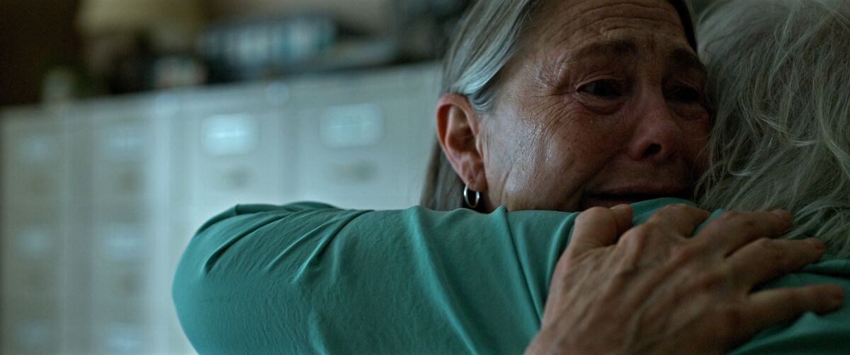 A woman with gray hair hugs a person who has their back to the camera.