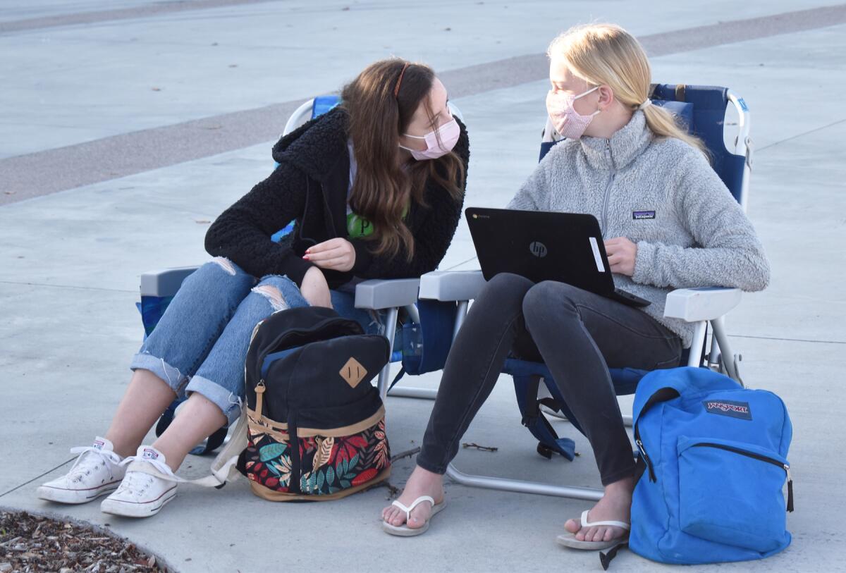 Two eighth-grade students sit in beach chairs outdoors.