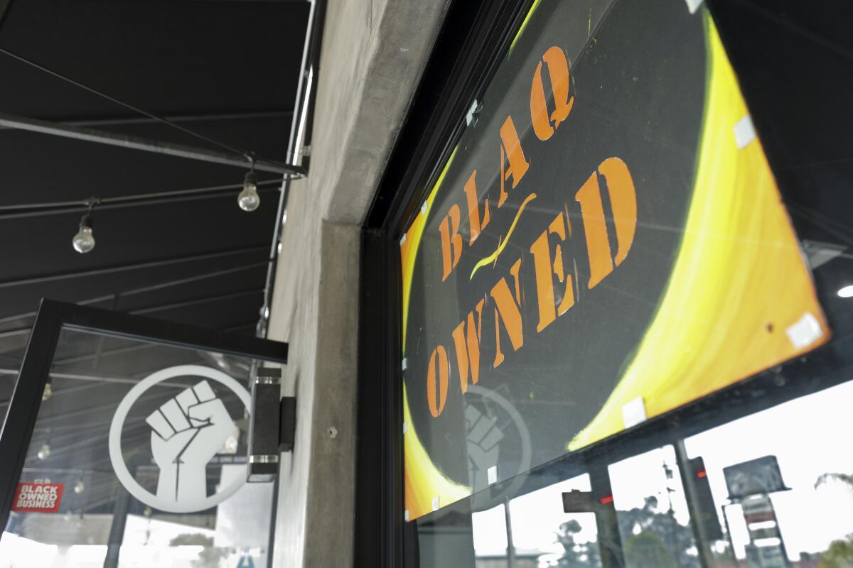 A photo of a yellow, black and orange sign reading, "BLAQ OWNED" on the front window of restaurant BlaqHaus.