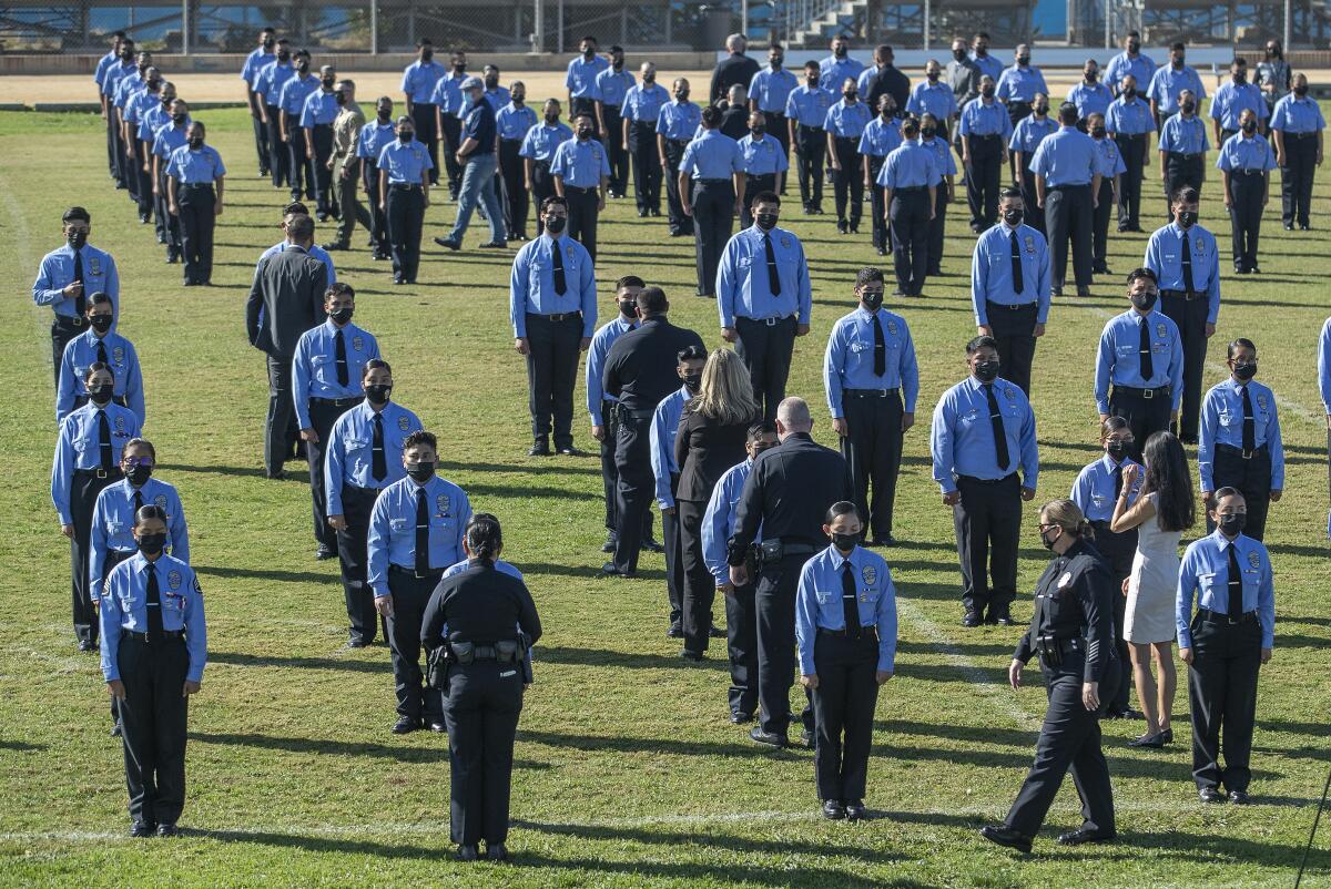 Cadets in uniform stand in a field as police officers look them over.