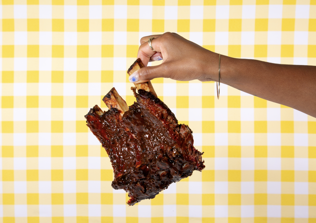 A hand holds a section of barbecued ribs by a bone