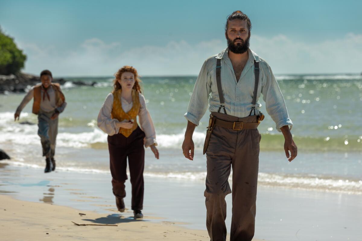 A boy, a woman and a man walk near the waves on a sunny beach.