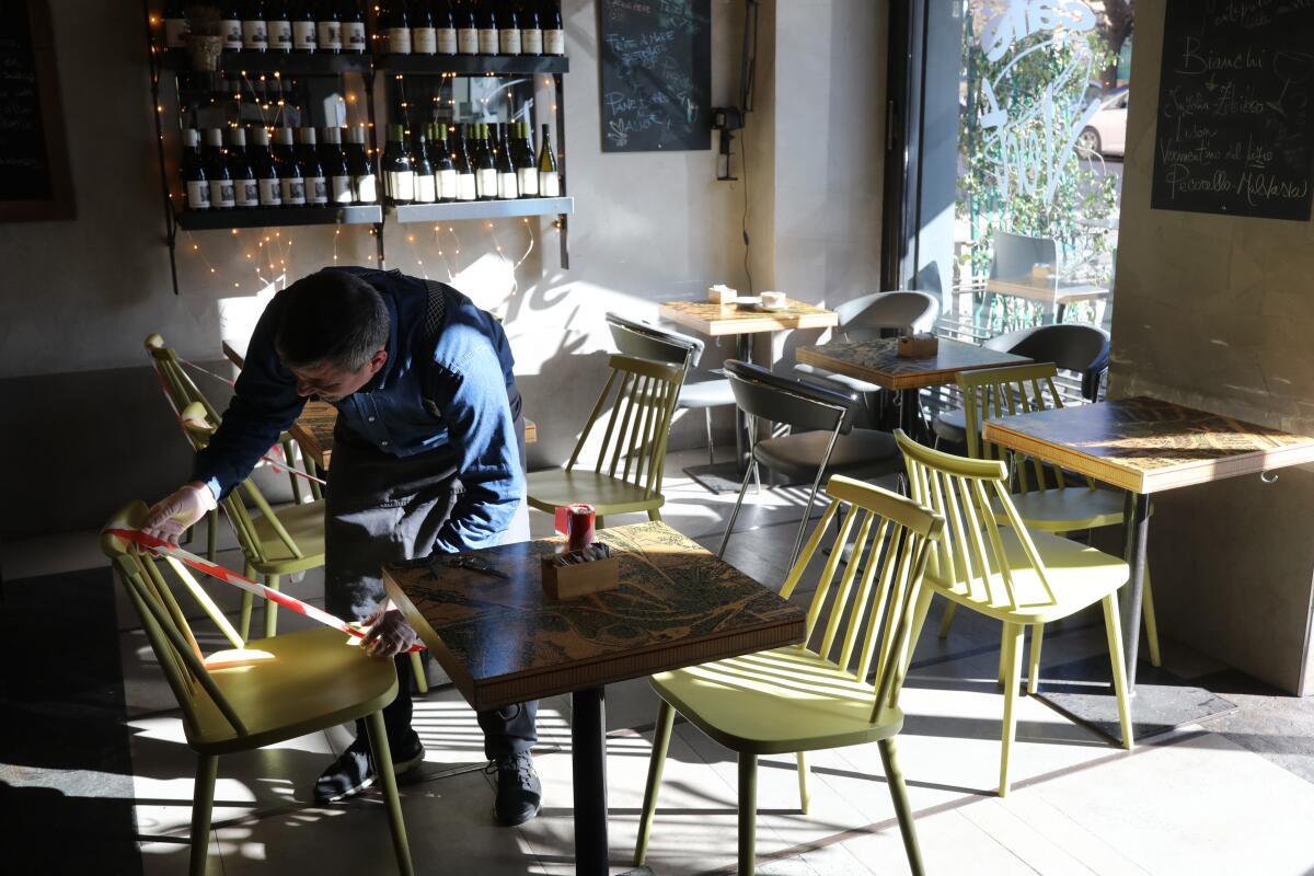 A waiter at a restaurant in Rome attaches tape to a chair to ensure that customers sit about 3 feet apart.