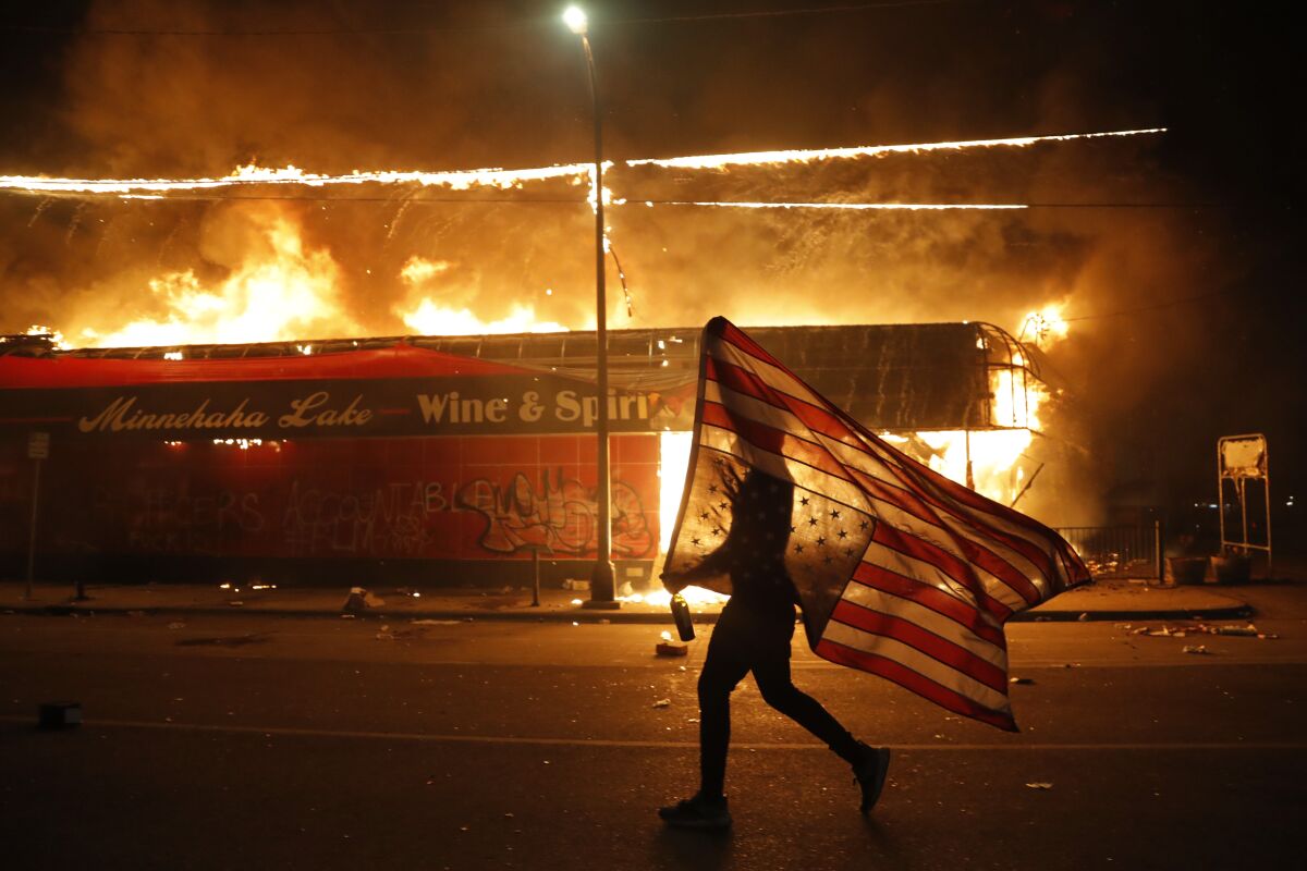 A protester carries a U.S. flag past a burning building in Minneapolis during a protest over the death of George Floyd