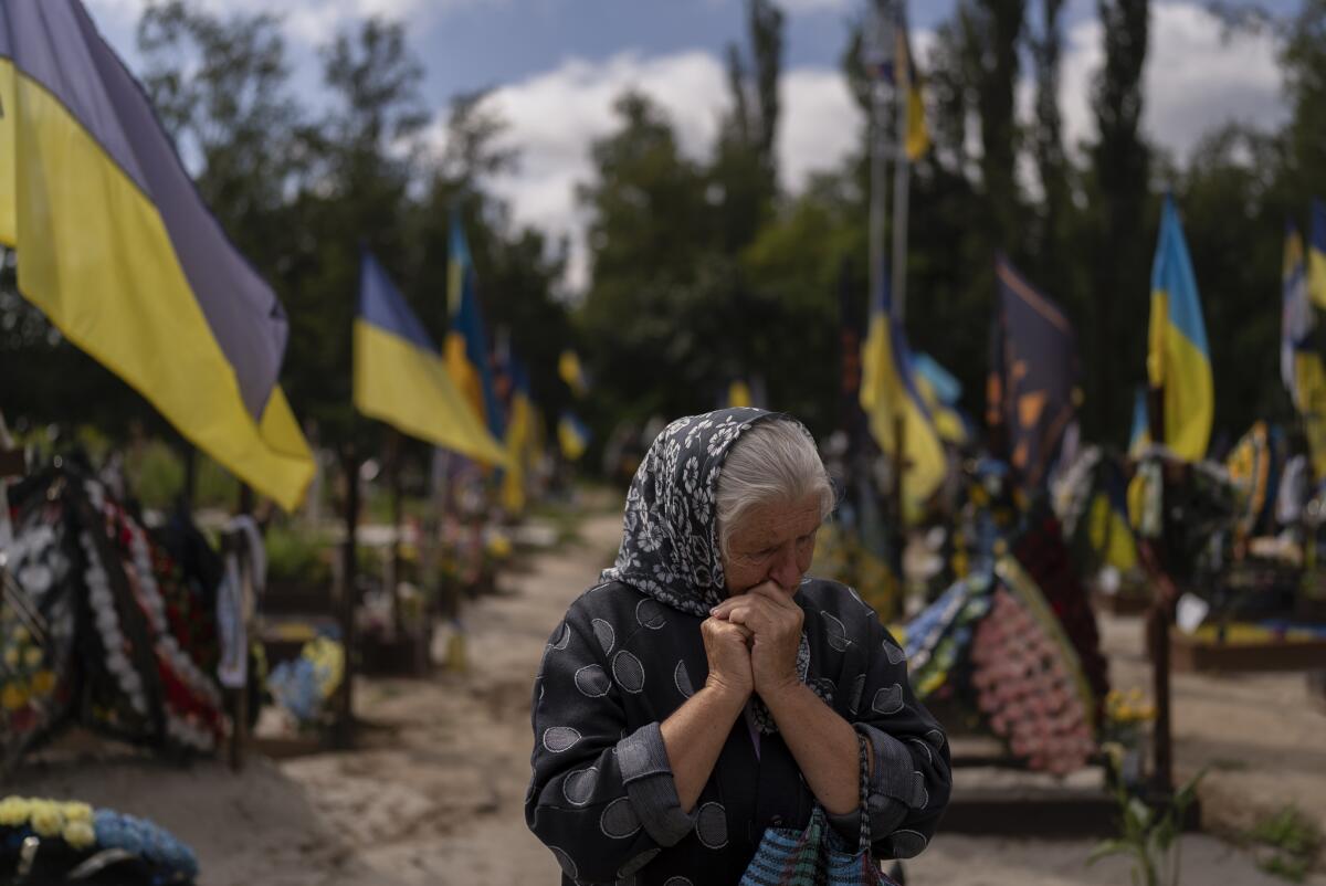 A woman sobs in a graveyard where Ukrainian flags stand. 