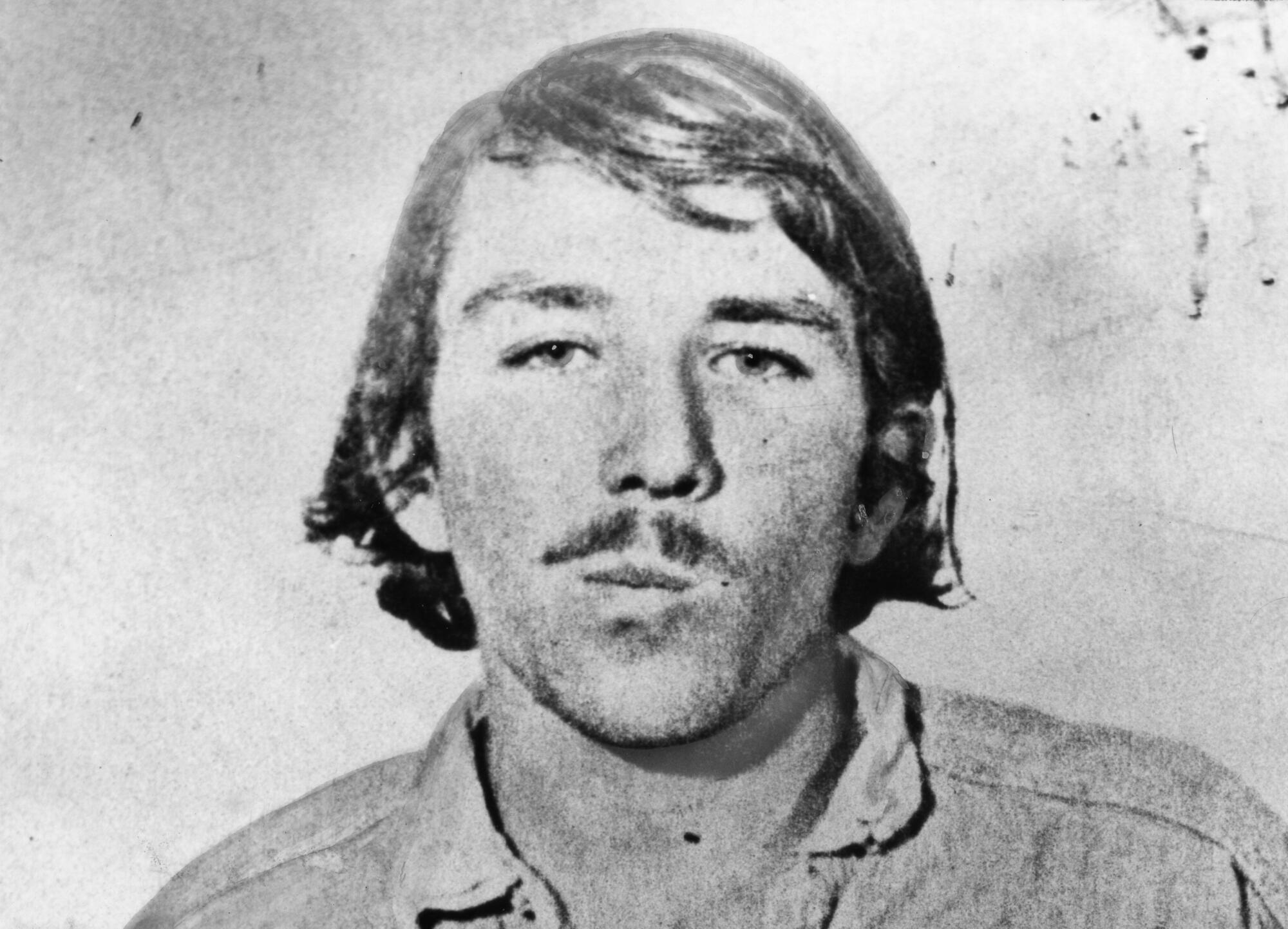 Booking photo of Andrew Daulton Lee in a mustache and hair down to his collar.