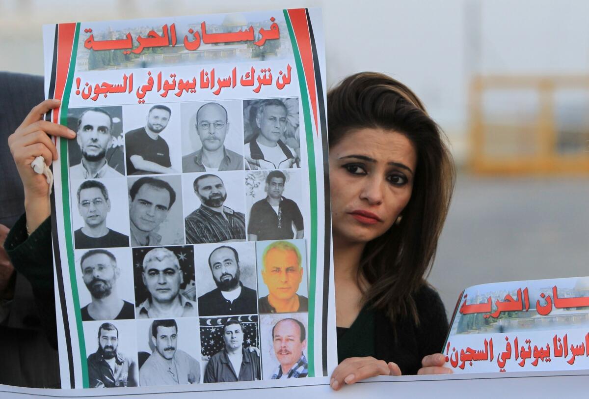 A Palestinian woman holds a poster Saturday bearing pictures of Arab detainees being held in Israeli prisons since before the 1993 Oslo peace accords. Palestinians were protesting the postponement of the release of the prisoners outside the gates of Ofer prison, near the West Bank town of Betunia.