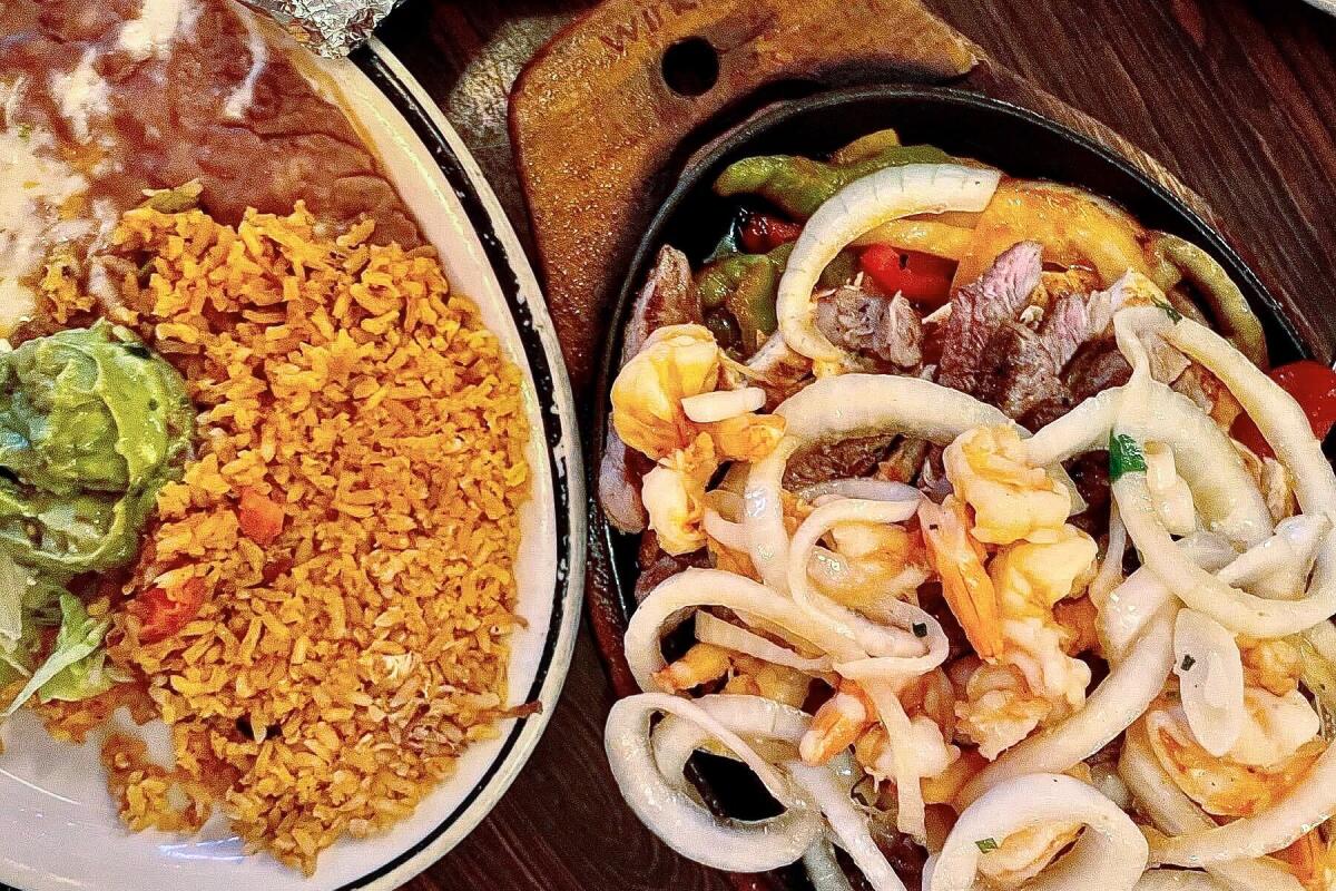 A platter of Parillada fajitas next to a platter of Mexican rice and beans.