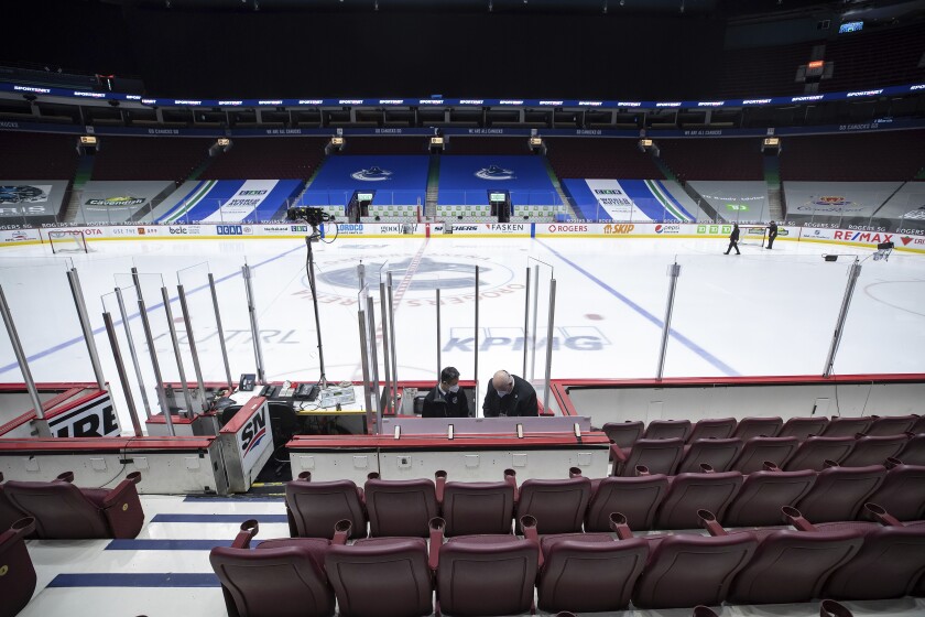 Off-ice officials pack up equipment after the Vancouver Canucks and Calgary Flames NHL hockey game was postponed due to a positive COVID-19 test result in Vancouver, British Columbia, Wednesday, March 31, 2021. (Darryl Dyck/The Canadian Press via AP)