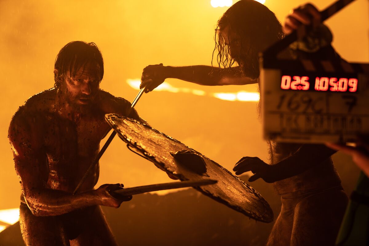 Two actors battle in front of a fiery background.